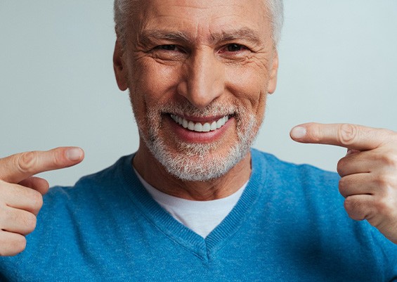 Man in blue shirt pointing to his smile with both hands
