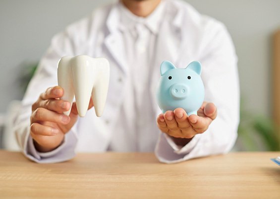 Man in white coat holding model tooth in one hand and blue piggy bank in the other hand