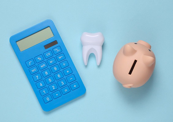 A calculator, a model tooth, and a piggy bank against a blue background