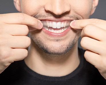 A smiling man putting a whitening strip on his teeth