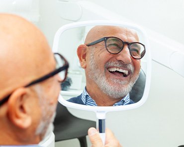 Mirror reflecting face of man with white beard and glasses