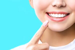 Nose-to-neck view of woman pointing to her bright white smile with a single finger